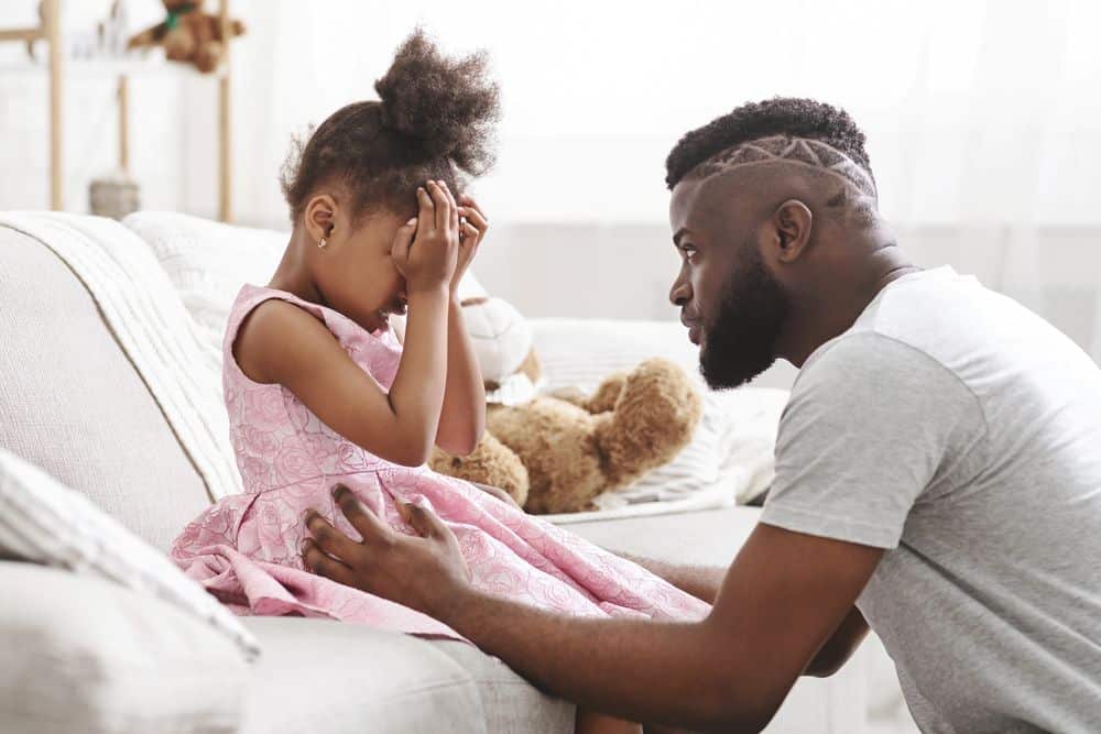 A father gently comforting his preschool daughter who is upset, teaching emotional support during a big feelings moment.
